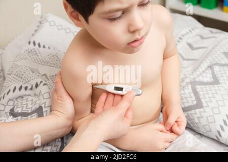 Una madre o un infermiere misura la temperatura di un ragazzo di 4 anni con un termometro elettronico Foto Stock