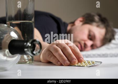 Un uomo si trova su un letto dopo una festa di alcol, tenendo in mano le pillole di hangover Foto Stock