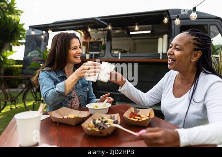 Amici anziani multirazziali felici che si divertono a mangiare in un mercato di camion Street food Foto Stock