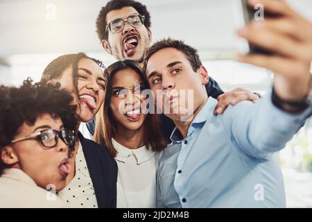 Provate a guardare ragazzi seri. Foto di un gruppo di colleghi di lavoro allegri che prendono insieme un autoritratto all'interno dell'ufficio durante il giorno. Foto Stock