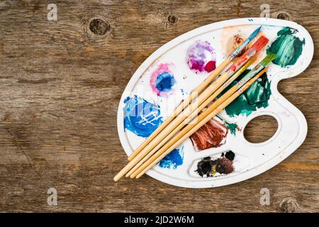 Strumenti di disegno in studio d'arte. Foto dall'alto di pennelli su palette d'arte. Artista vecchio tavolo in legno con accessori. Foto Stock