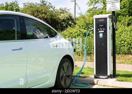 Woodbridge Suffolk UK Maggio 18 2022: Una Tesla Model 3 per la ricarica di auto elettriche presso la stazione di ricarica plug-in in un parcheggio pubblico a Suffolk, Regno Unito Foto Stock