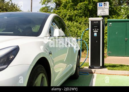 Woodbridge Suffolk UK Maggio 18 2022: Una Tesla Model 3 per la ricarica di auto elettriche presso la stazione di ricarica plug-in in un parcheggio pubblico a Suffolk, Regno Unito Foto Stock