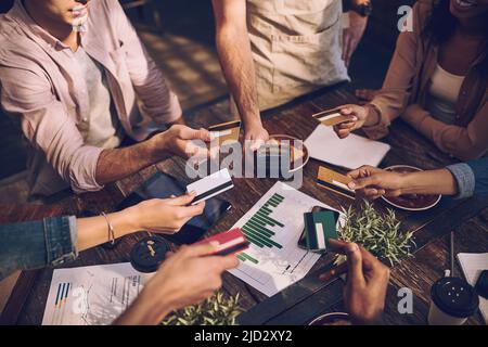 Con quel bonus, erano tutti disposti a pagare. Scatto ritagliato di un gruppo di colleghi che tengono fuori le loro carte bancarie per pagare il conto in un bar. Foto Stock