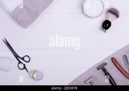 Diversi vecchi rasoi vintage, schiuma, asciugamani, forbici e spazzola su uno sfondo bianco di legno. Visualizza dall'alto spazio per il testo Foto Stock