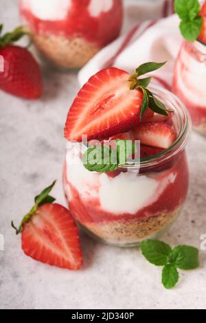 Cheesecake alla fragola. Cheesecake o trifle con fragola in vetro su sfondo vecchio tavolo grigio cemento. Cheesecake senza cottura. Dess Foto Stock