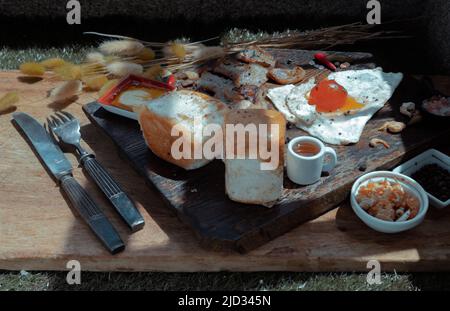 Colazione fatta in casa con uova fritte, pancetta fritta e toast serviti con miele su tagliere di legno. Concetto di cibo sano, fuoco selettivo. Foto Stock