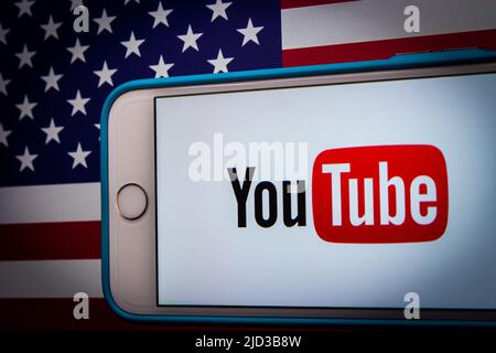 Kumamoto, GIAPPONE - Feb 22 2022 : l'immagine concettuale del logo di YouTube su un iPhone su sfondo di una bandiera americana in un umore scuro Foto Stock