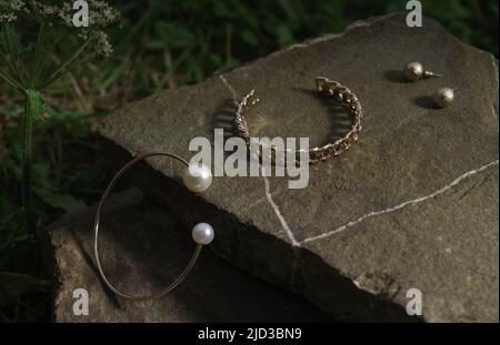 Il bracciale dorato perla e il bracciale a catena con orecchini dorati si abbinano su una roccia in natura Foto Stock