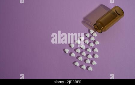 Pillole a forma di cuore versate da flacone Medicine su sfondo viola con spazio copia Foto Stock