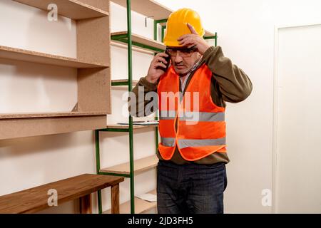 Ispettore caucasico maturo che parla al telefono cellulare mentre controlla lo stato e l'avanzamento del lavoro in ufficio. Concetto di organizzazione del lavoro, Foto Stock