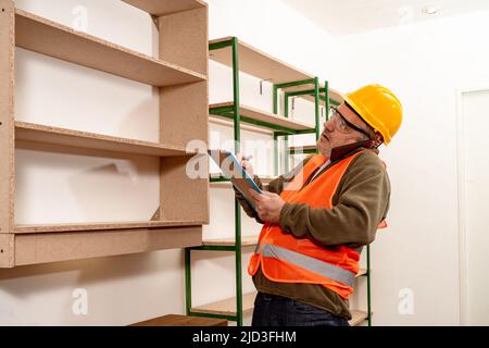 Ispettore caucasico maturo che parla al telefono cellulare mentre controlla lo stato e l'avanzamento del lavoro in ufficio. Concetto di organizzazione del lavoro, Foto Stock