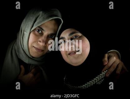 Due donne musulmane felici in abbraccio insieme su sfondo nero. Foto di alta qualità Foto Stock