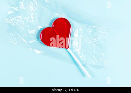 Lollipop a forma di cuore rosso su confezione trasparente su sfondo blu. Vista dall'alto. Foto Stock