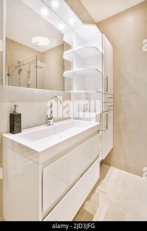 Lavandino con rubinetto e sapone liquido appeso su una parete piastrellata sotto lo specchio in bagno contemporaneo a casa Foto Stock