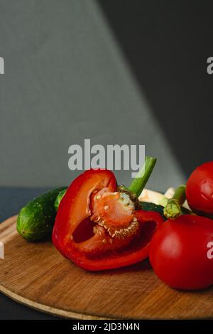 rami di asparagi verdi freschi, peperoni, pomodori e cetrioli su un asse di legno, sfondo grigio scuro, vista dall'alto. Concetto di trend di base con copia sp Foto Stock