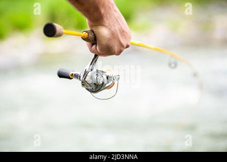 Attrezzi da pesca. Rifornimenti di pesce ed attrezzatura. I pescatori si avvicinano sullo sfondo del fiume. Pescatore mano che tiene canna da pesca con mulinello Foto Stock