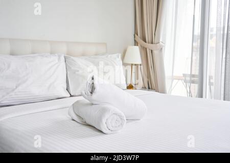 asciugamani bianchi arrotolati sul letto dell'hotel. Foto Stock