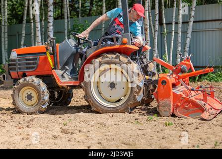 Un agricoltore su un mini trattore allenta il terreno per il prato. Coltivazione di terra, livellamento di superficie. Foto Stock