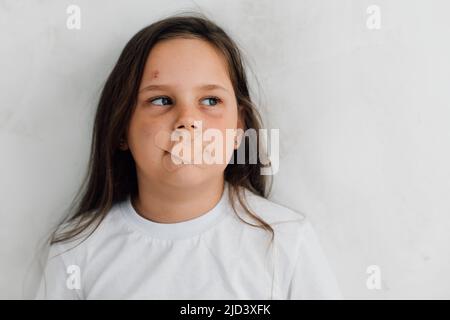 ritratto di piccola ragazza contusa con capelli lunghi che chiedono aiuto. Sigillato in bocca con cerotti medici. Foto Stock