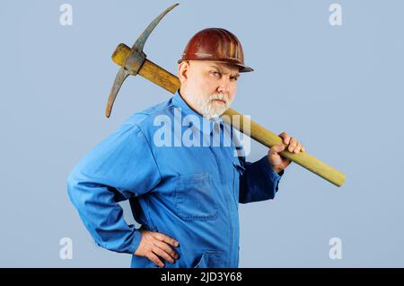 Operaio di costruzione con piccone. Uomo da lavoro con bearded con pick-ax. Appaltatore in elmetto con pickax. Foto Stock