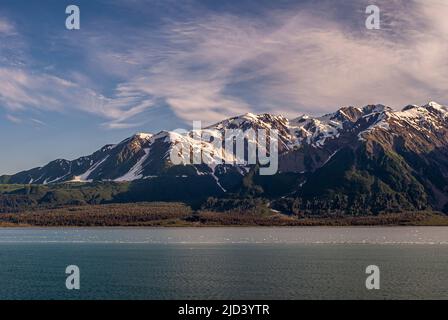 Disincantment Bay, Alaska, USA - 21 luglio 2011: Paesaggio con neve coperta scura catena montuosa sotto blu cielo nuvoloso dietro azzurro oceano acqua con Foto Stock