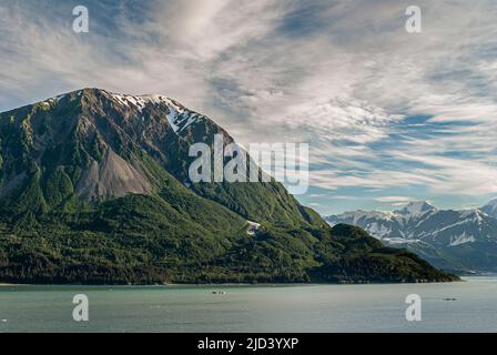 Disincantment Bay, Alaska, USA - 21 luglio 2011: Torri di montagna verde boschive su acqua dell'oceano verdeggiante sotto il paesaggio azzurro. Montagna innevata Foto Stock