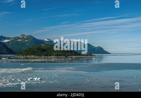 Disincantment Bay, Alaska, USA - 21 luglio 2011: Ampio paesaggio che si affaccia sull'oceano sotto il paesaggio azzurro con isolotto boscoso e montagne in orizzonte Foto Stock