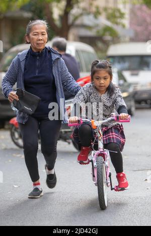 Una ragazza indonesiana e sua nonna vestita in primavera a tema una bicicletta BTWIN rosa in primavera sulla strada di un complesso di appartamenti a Shanghai Foto Stock