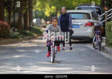 Una ragazza indonesiana e sua nonna vestita in primavera a tema una bicicletta BTWIN rosa in primavera sulla strada di un complesso di appartamenti a Shanghai Foto Stock