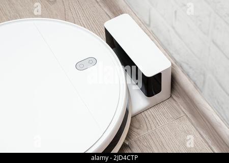 Il moderno aspirapolvere robot si sta caricando vicino alla docking station. Tecnologie moderne per aiutare una casalinga Foto Stock