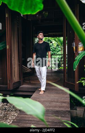 giovane uomo che cammina su un sentiero di legno dal piccolo ingresso tropicale casa a bali indonesia Foto Stock