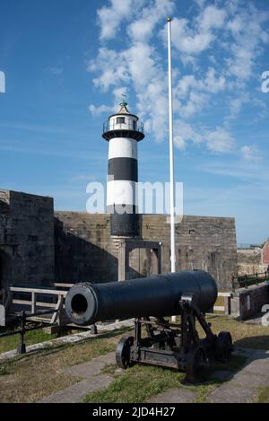 Un vecchio cannone situato all'ingresso del Castello di Southsea a Portsmouth, Inghilterra. Il faro dei castelli si trova dietro di esso. Foto Stock