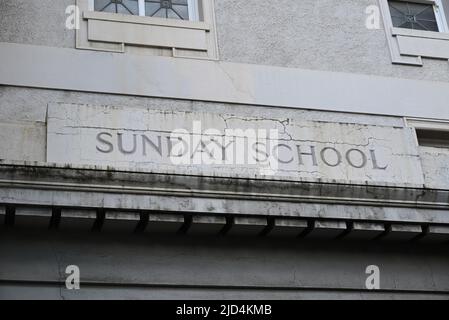 Domenica segno scuola, circondato da crepe, inciso nella parete bianca usurata di un vecchio edificio Foto Stock