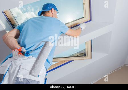 Lavoro caucasico applicazione di tocchi di finitura sugli angoli intorno alla finestra verniciatura con vernice bianca utilizzando un piccolo pennello. Preparazione di Apartme Foto Stock