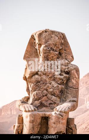 Antico Colossi Egiziano di pietra Memnon statua del faraone con sfondo di montagna alla Valle dei Re a Luxor Foto Stock