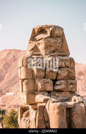 Antico Colossi Egiziano di pietra Memnon statua del faraone con sfondo di montagna alla Valle dei Re a Luxor Foto Stock