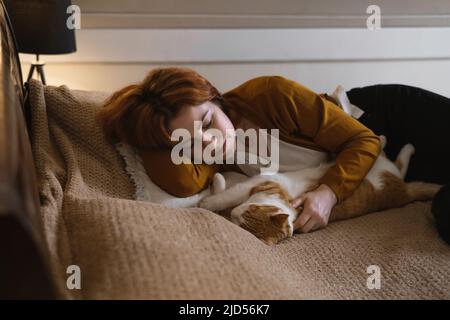 Donna di mezza età che tiene gatto zenzero carino. Femmina che abbraccia il suo bel gattino capelli corti in camera da letto la sera. Spazio di copia. Adorabile animale domestico Foto Stock