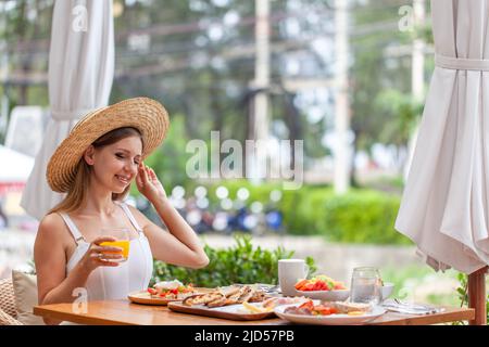 Giovane donna sorridente a colazione nel ristorante all'aperto dell'hotel. Vacanze estive Foto Stock
