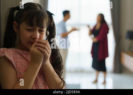 La violenza familiare e il concetto di conflitto familiare, triste bambina con sfocatura di madre che combatte padre con litigio a casa. Foto Stock