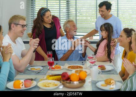 Buona multietnia e famiglia multigenerazione che festeggia il compleanno dei nonni nel soggiorno di casa. Foto Stock
