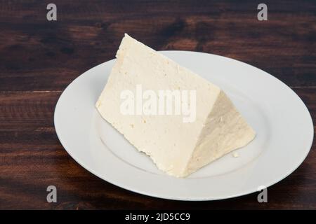 Piatto con pezzo di formaggio bianco; foto su sfondo di legno. Foto Stock