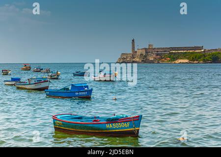 Piccole barche ormeggiano nell'acqua della Baia di l'Avana con il famoso punto di riferimento dell'Avana, la fortezza di El Morro sullo sfondo Foto Stock