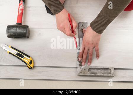 Il maestro femminile disegna una linea a matita sulla tavola, installando pavimenti in vinile al quarzo, lavori di installazione. Foto Stock