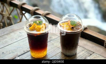 Due tazze con bevande salutari nella caffetteria all'aperto. Detox bevande fredde in moderno caffè con vista cascata. Bevande ghiacciate all'arancia, alla cannella e alla menta. Foto Stock