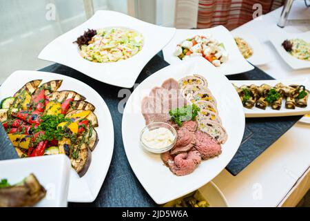 Tavolo a buffet con antipasti e insalate. Piatto di carne: Arrosto di manzo, lingua di manzo, tacchino e rotolo di verdure. Melanzane alla griglia, peperoni alla griglia, con Foto Stock