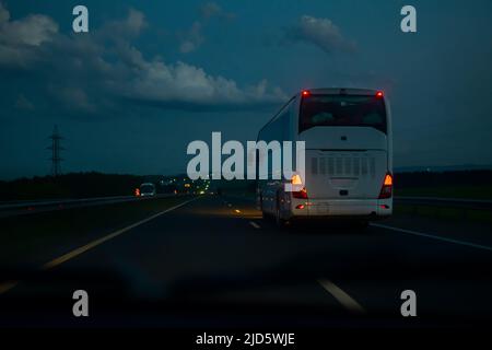 una vista di un autobus bianco passeggeri che viaggia lungo l'autostrada su una strada notturna a velocità dal lato di una macchina che la sorpasso al crepuscolo nel traffico Foto Stock