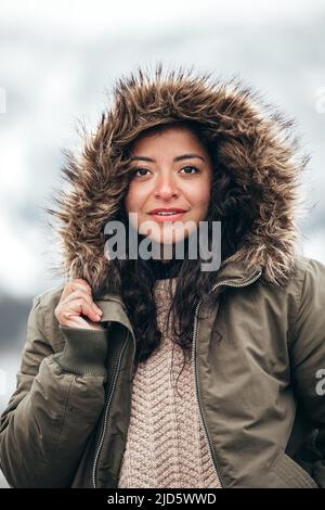 giovane ispanica donna in pelliccia verde giacca parka in inverno freddo con sfondo di montagna sfocato Foto Stock