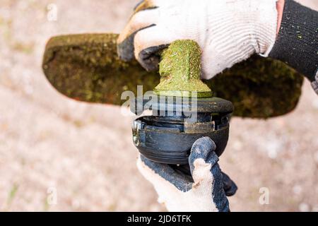 Un giardiniere rimuove una testina di taglio da un rasaerba alla linea di filettatura. Falciatura primaverile dell'erba. Foto Stock