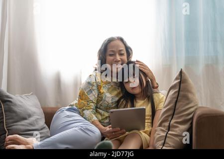 Ritratto asiatico, nonna e nipote che fanno attività ricreative giocando computer tablet sul divano Foto Stock